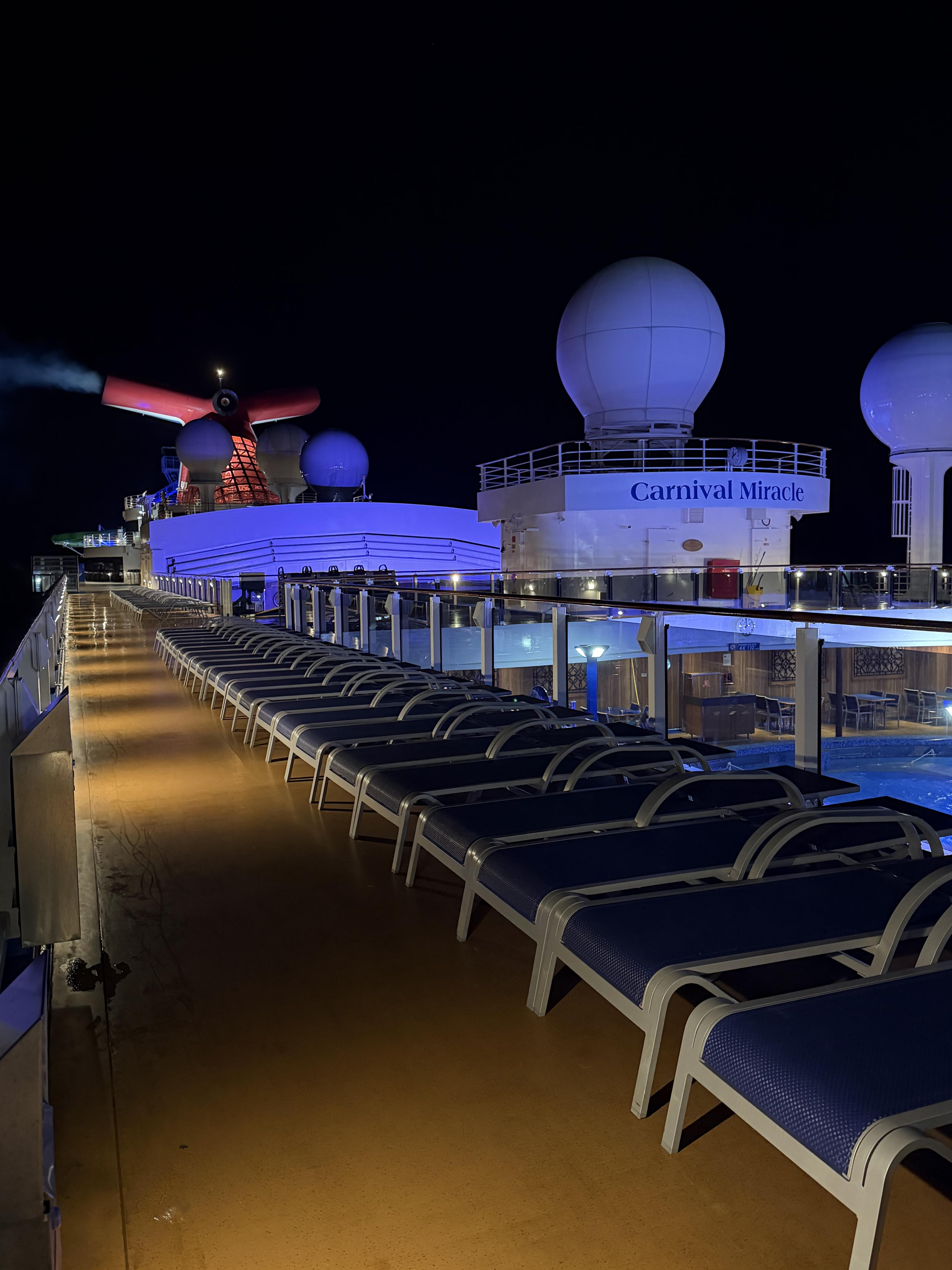 Night deck on Carnival Miracle — empty lounge chairs, moody blue lighting